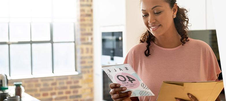 A woman reading a direct mail advertising piece promoting a sale.